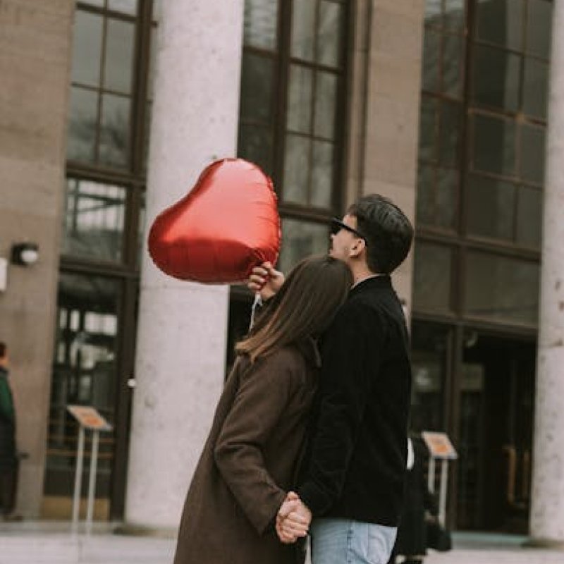 A couple is stading next to each other and holding a big heart shaped baloon.